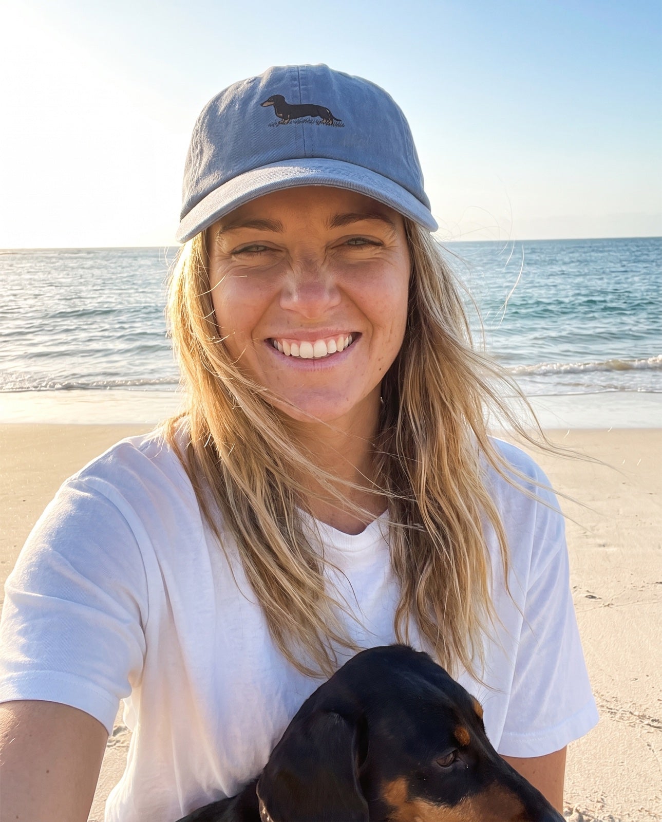 Mia wearing the washed-blue Dachshund Cap with her dachshund at the beach