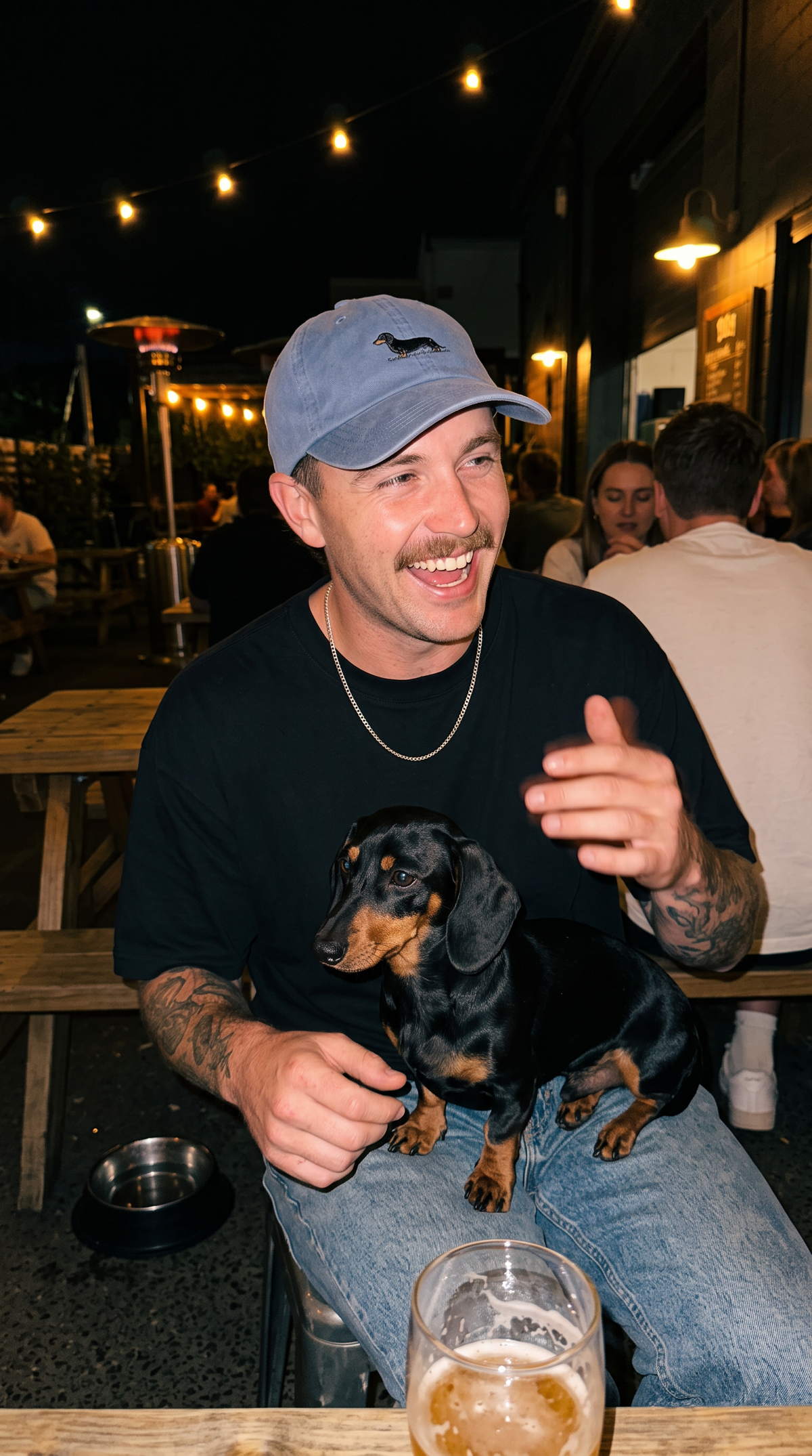 Man wearing the washed-blue Dachshund Cap while holding a black-and-tan dachshund